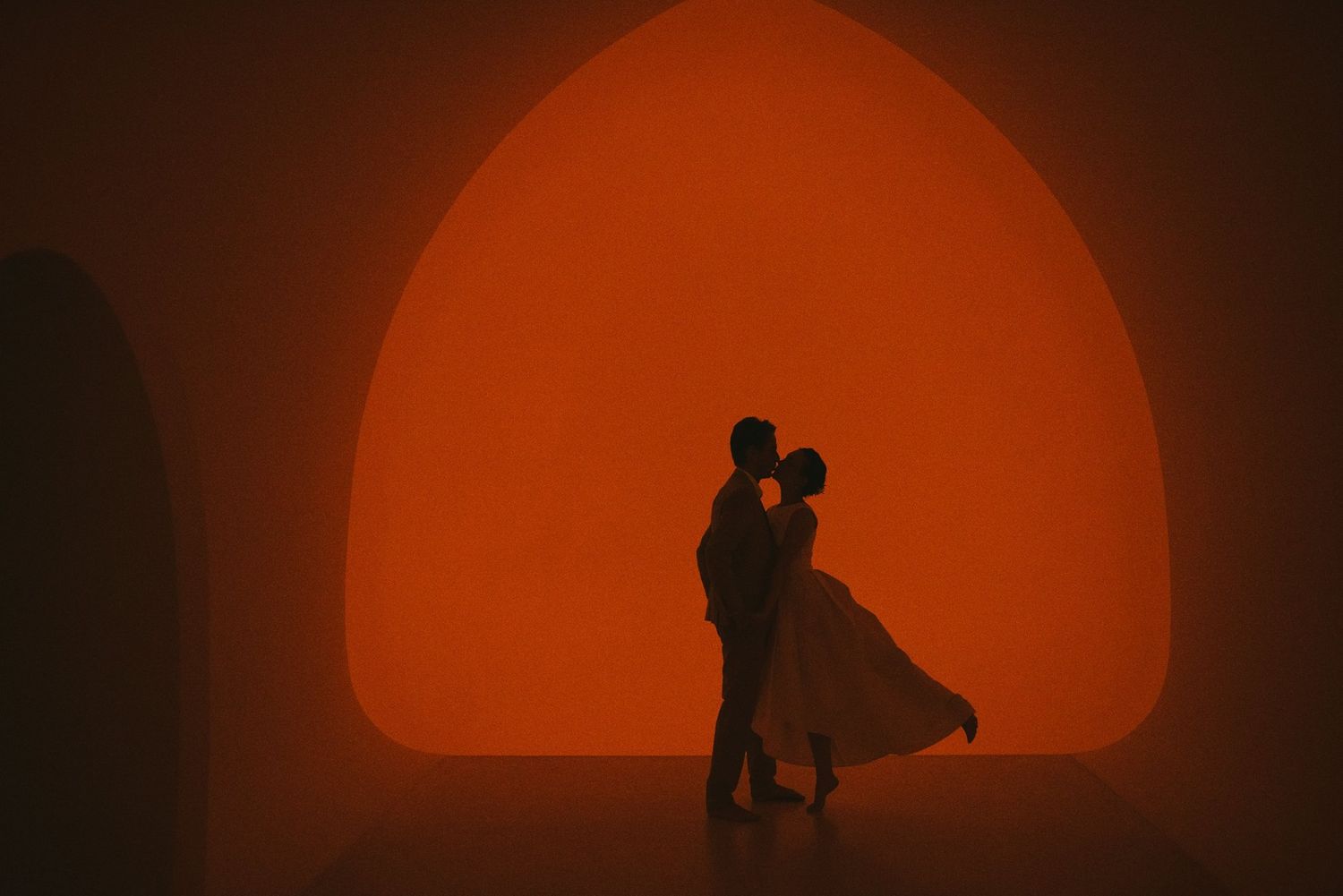 A romantic silhouette of a couple dancing against a warm orange archway backdrop.