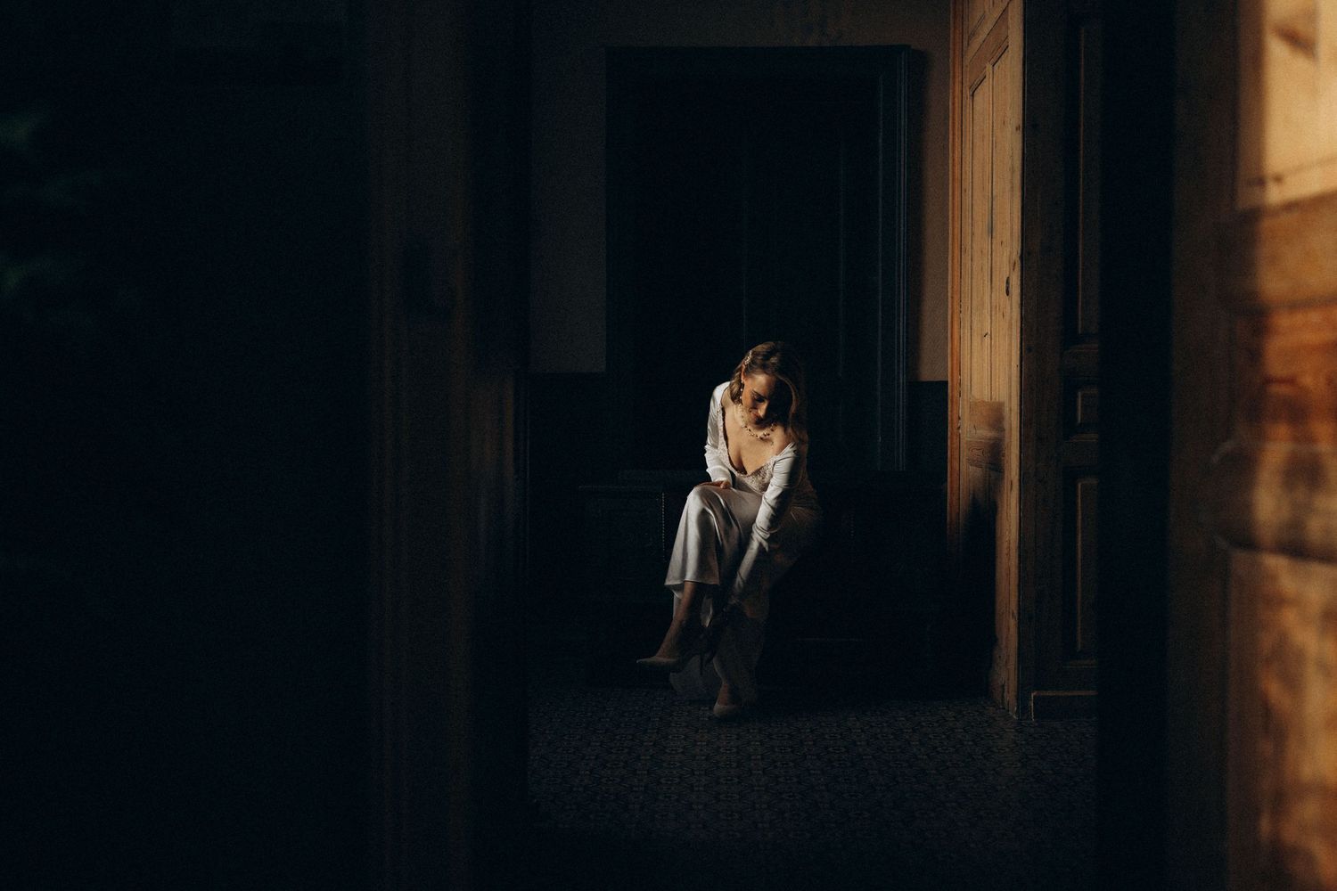 A dark and moody wedding scene shows silhouettes against dramatic window lighting in a rustic wooden interior.