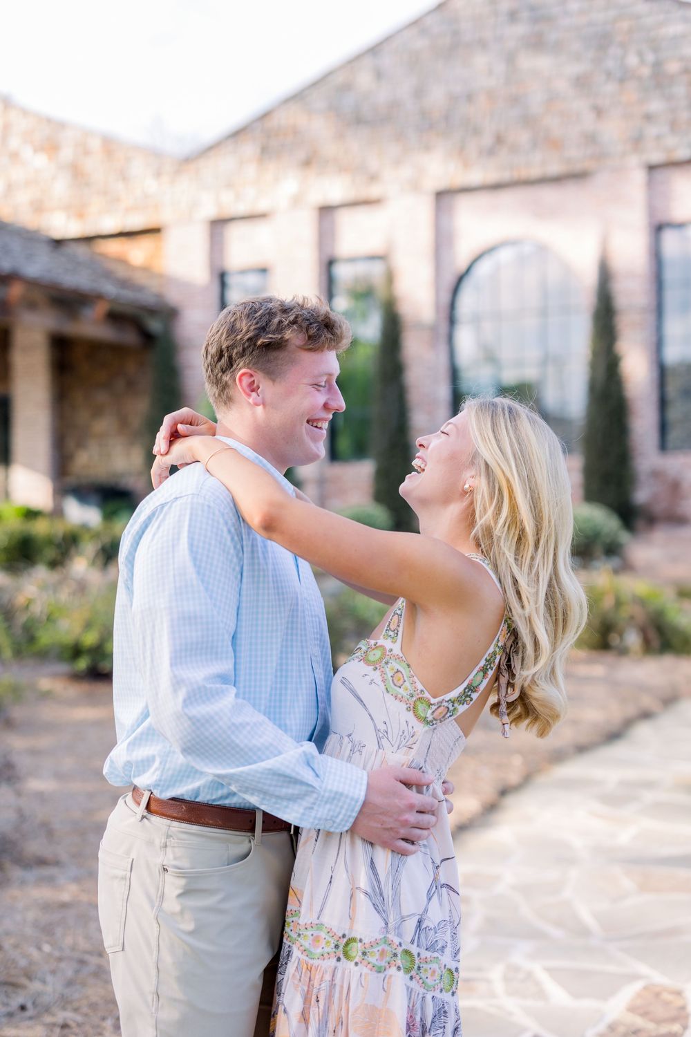 A couple shares joyful moments together on a stone patio with rustic buildings in the background.