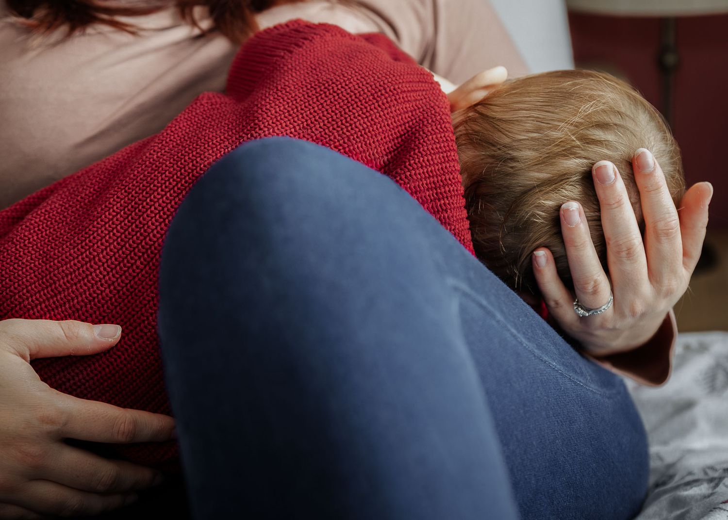 A mother tenderly holds her son's head and body as she breastfeeds him on the bed. Natural in home Bristol baby photography