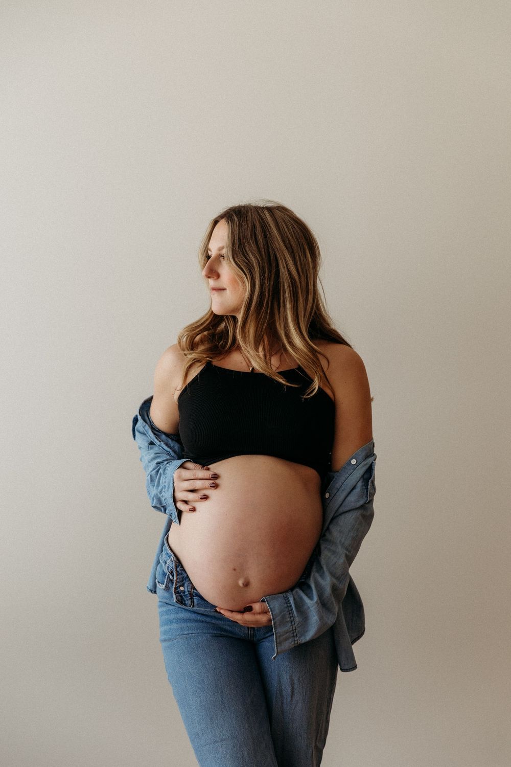 Pregnant woman standing in her Cleveland home, hands resting on belly during in-home maternity session