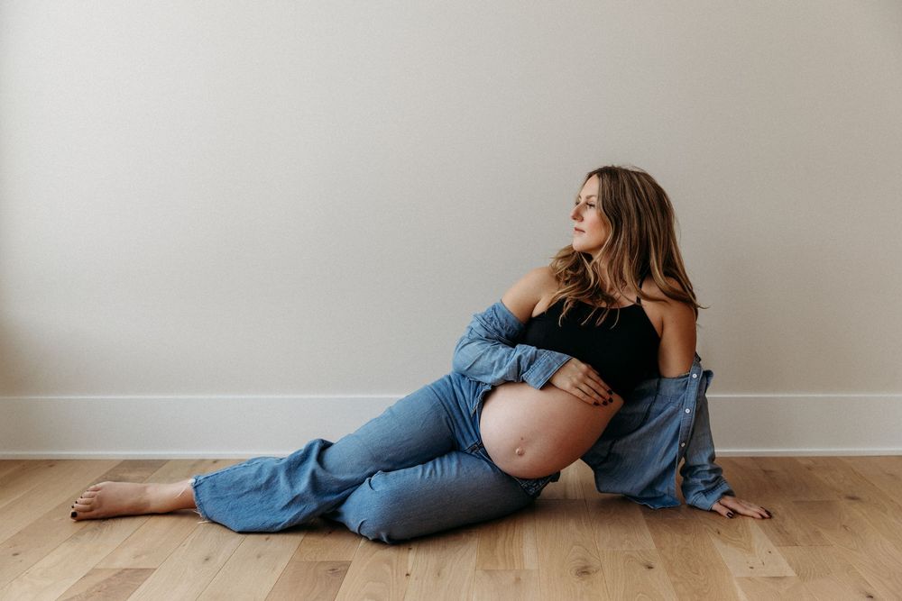 Artistic maternity photoshoot showing intimate moments on hardwood floor in natural light.
