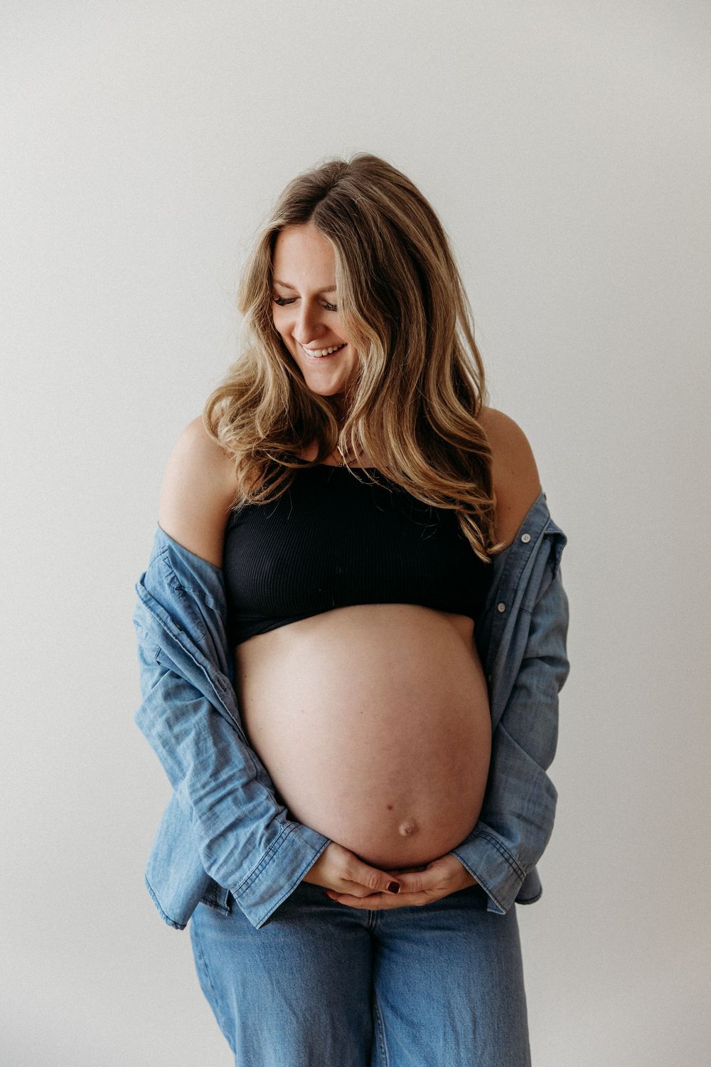 Close-up maternity photos showing pregnant belly with denim jacket in minimalist setting.