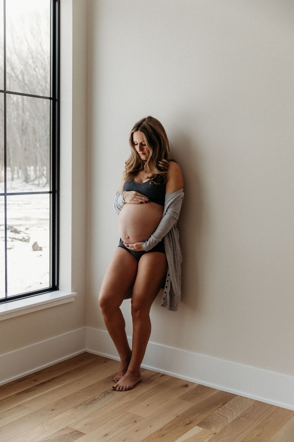 Intimate maternity portraits by window showing pregnancy journey in casual setting.