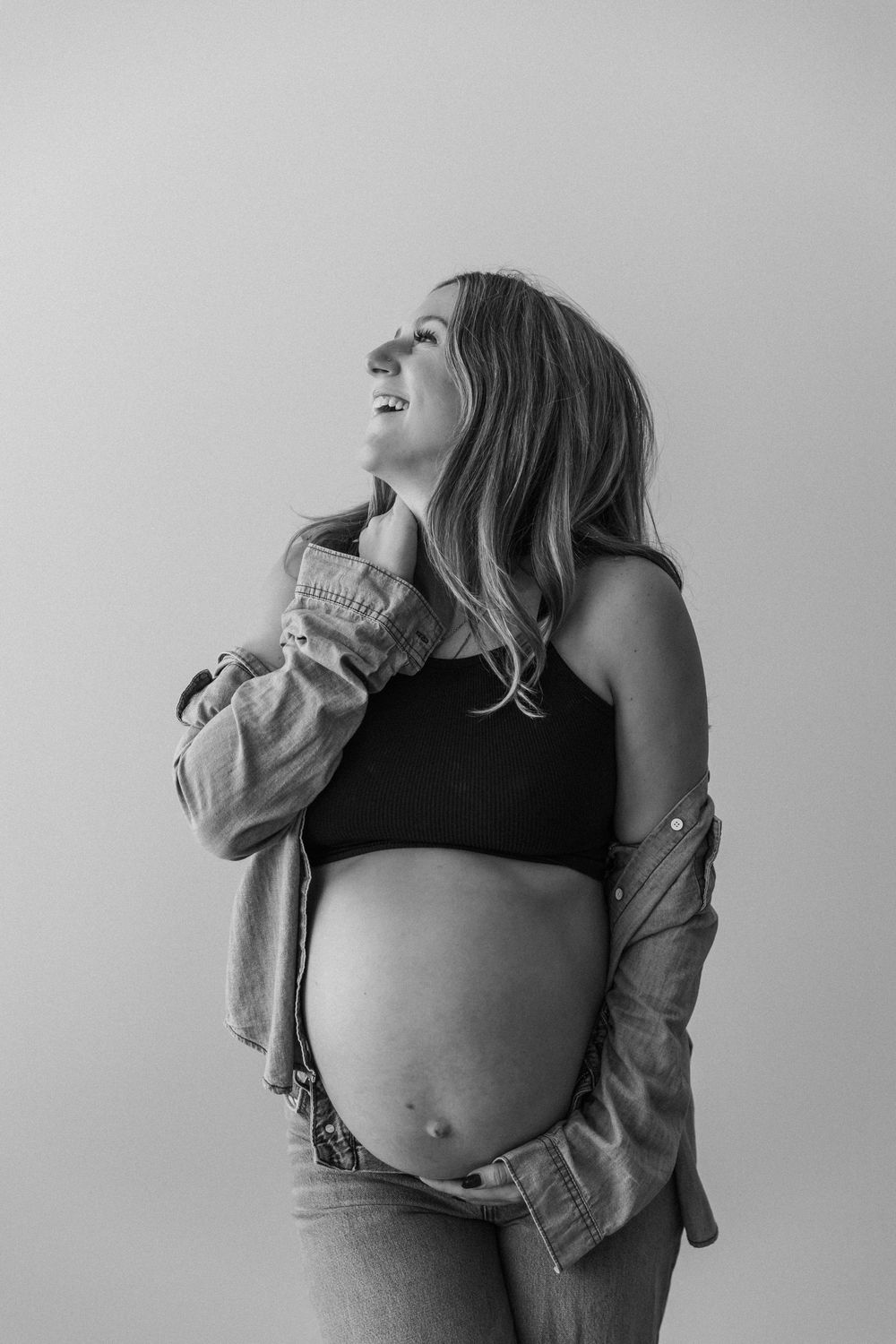 Black and white maternity portrait showing bare pregnant belly with denim jacket.