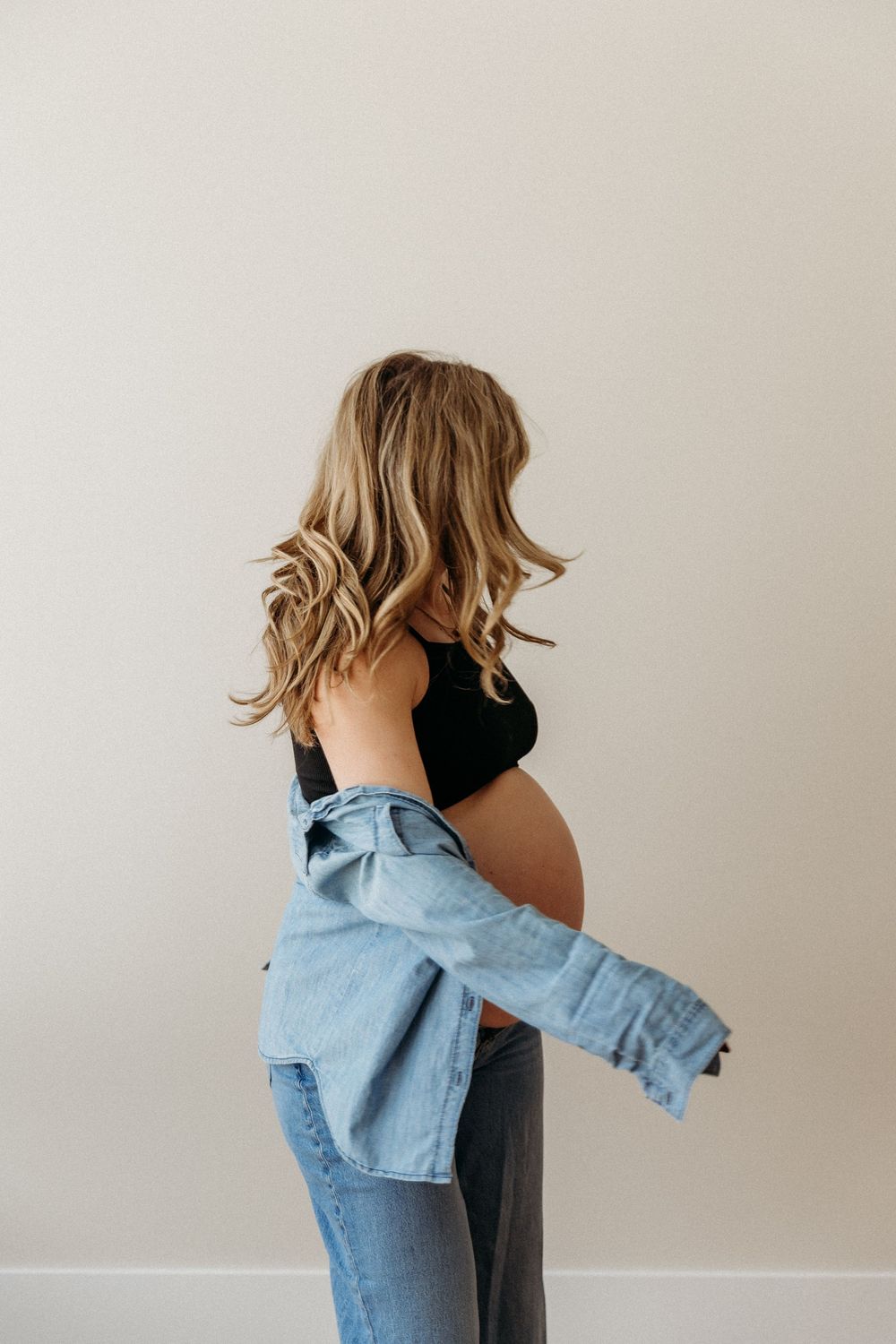 Side view of a pregnant figure in jeans and denim jacket against neutral background.