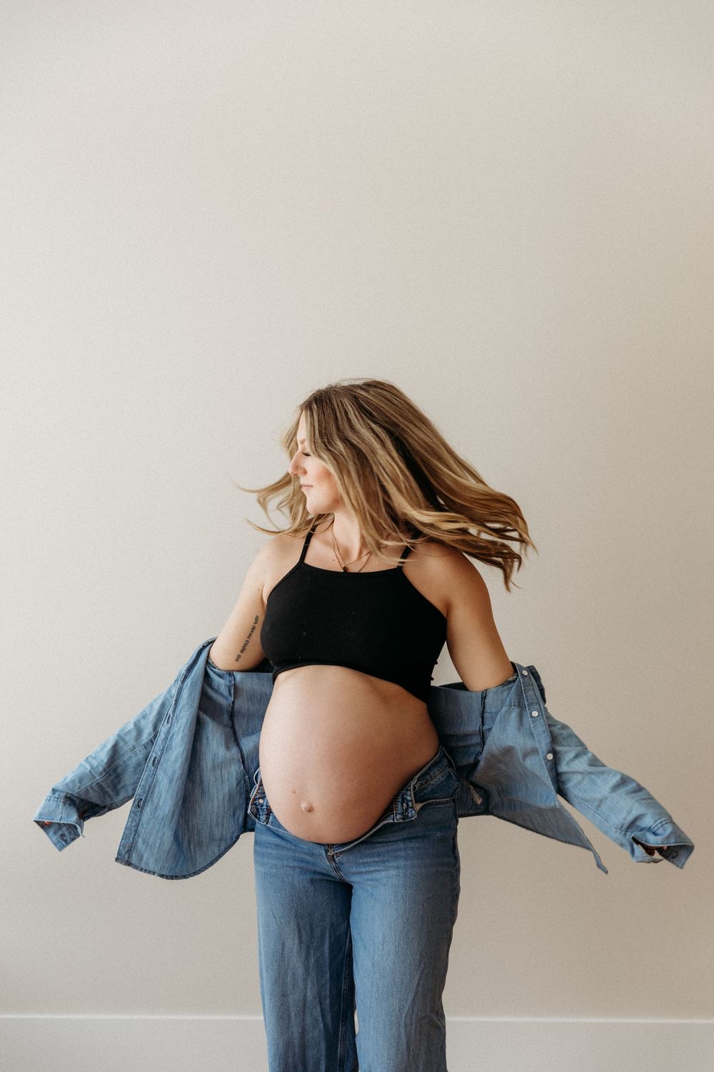 Dynamic maternity poses showing movement in denim and black against white wall.