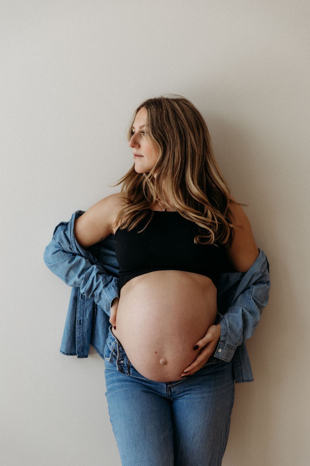 Natural maternity portraits featuring bare belly with casual denim styling.
