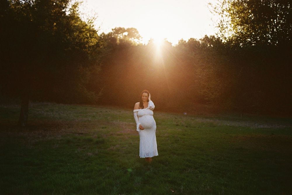 A person stands in a sunlit field at golden hour with sun flare creating a dreamy backlit silhouette effect.