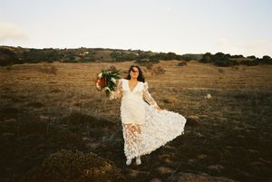 Couple in elegant wedding attire walks hand in hand across a scenic golden field at sunset.