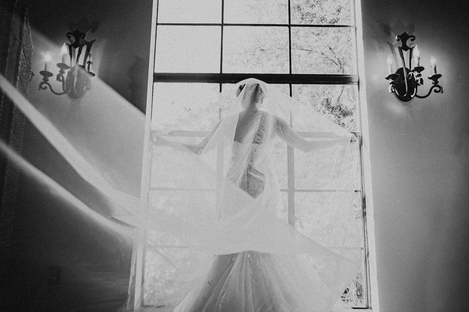 Artistic black and white wedding dress details showing gown hanging with chandelier lighting in elegant setting.