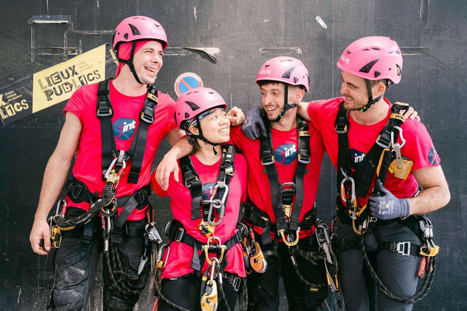 A group of climbers wearing pink helmets and red shirts prepare their safety gear and harnesses for an adventure.