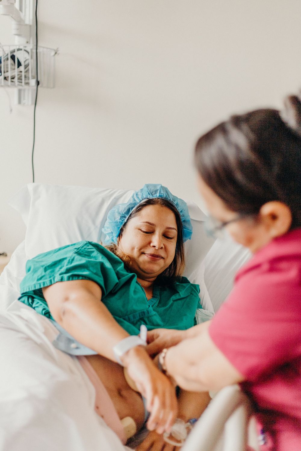 Medical staff member in pink scrubs providing care to a patient lying in a hospital bed.