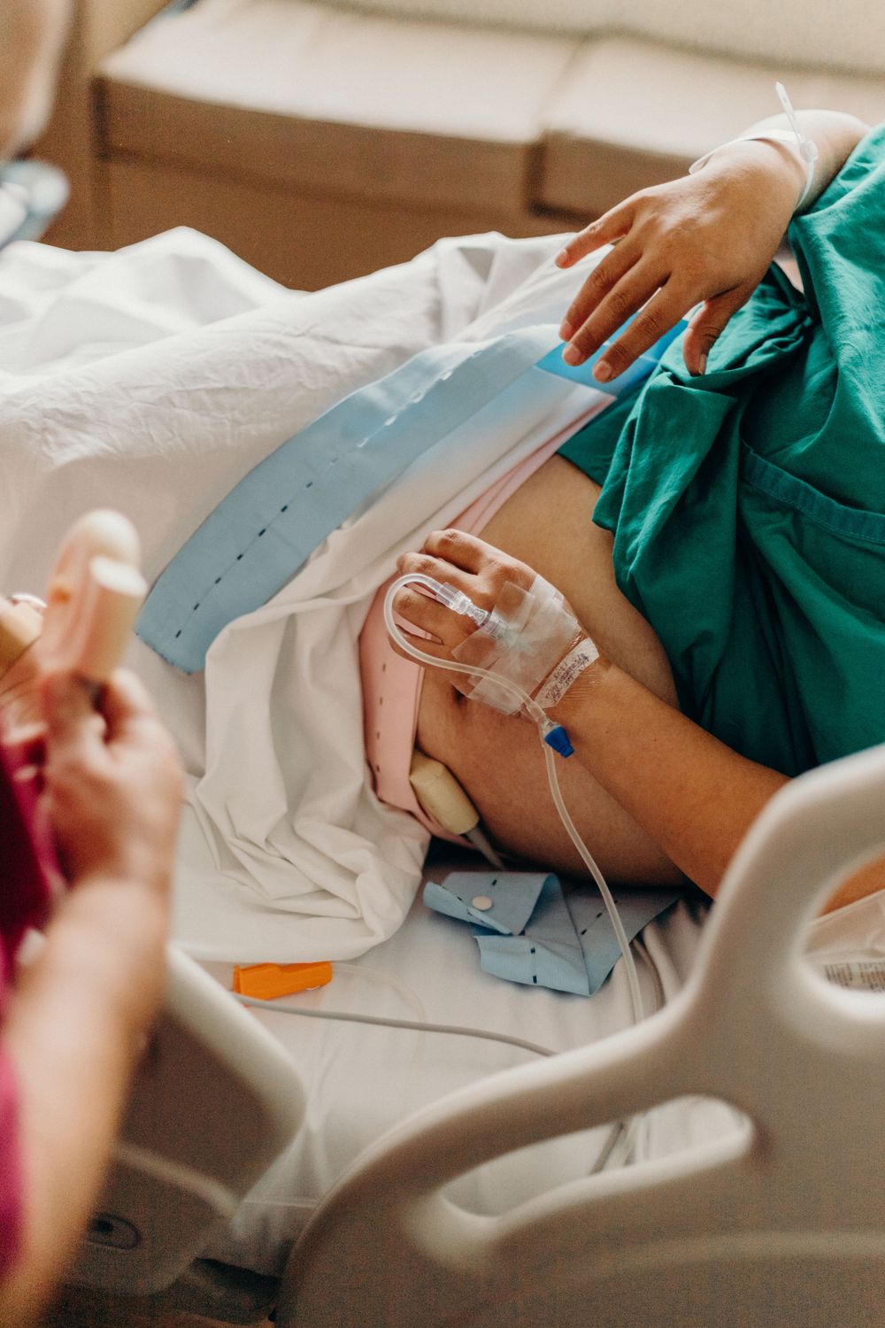 Patient in hospital gown receives medical treatment with IV drip and monitoring equipment.