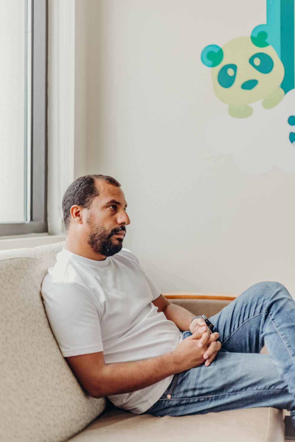 Person relaxing on a couch while using a mobile device against a wall with panda decorations.