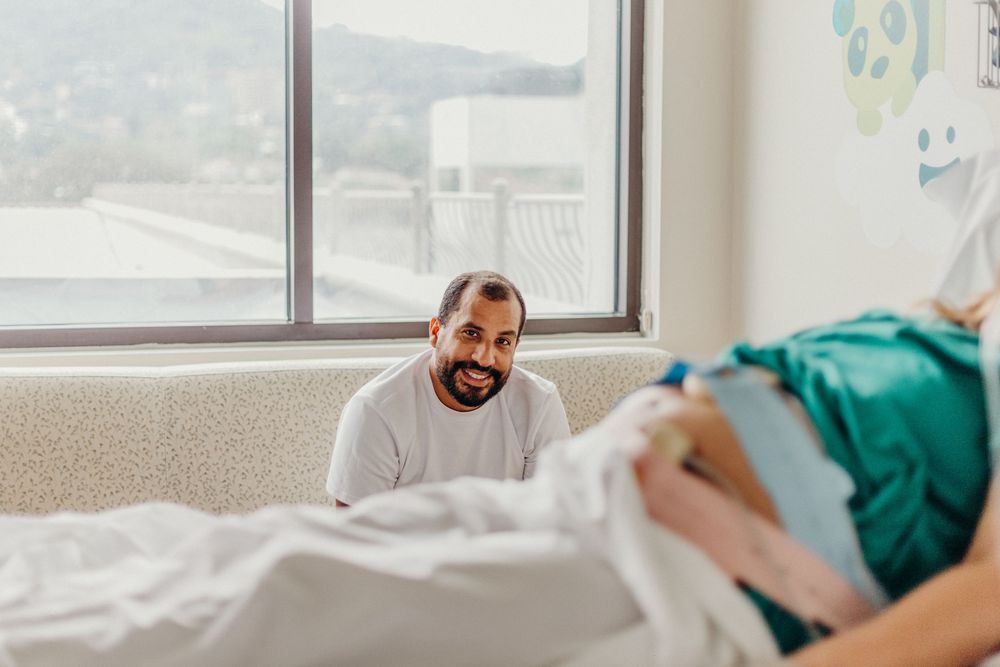 Healthcare worker in scrubs attending to a patient in a hospital bed during a medical procedure.