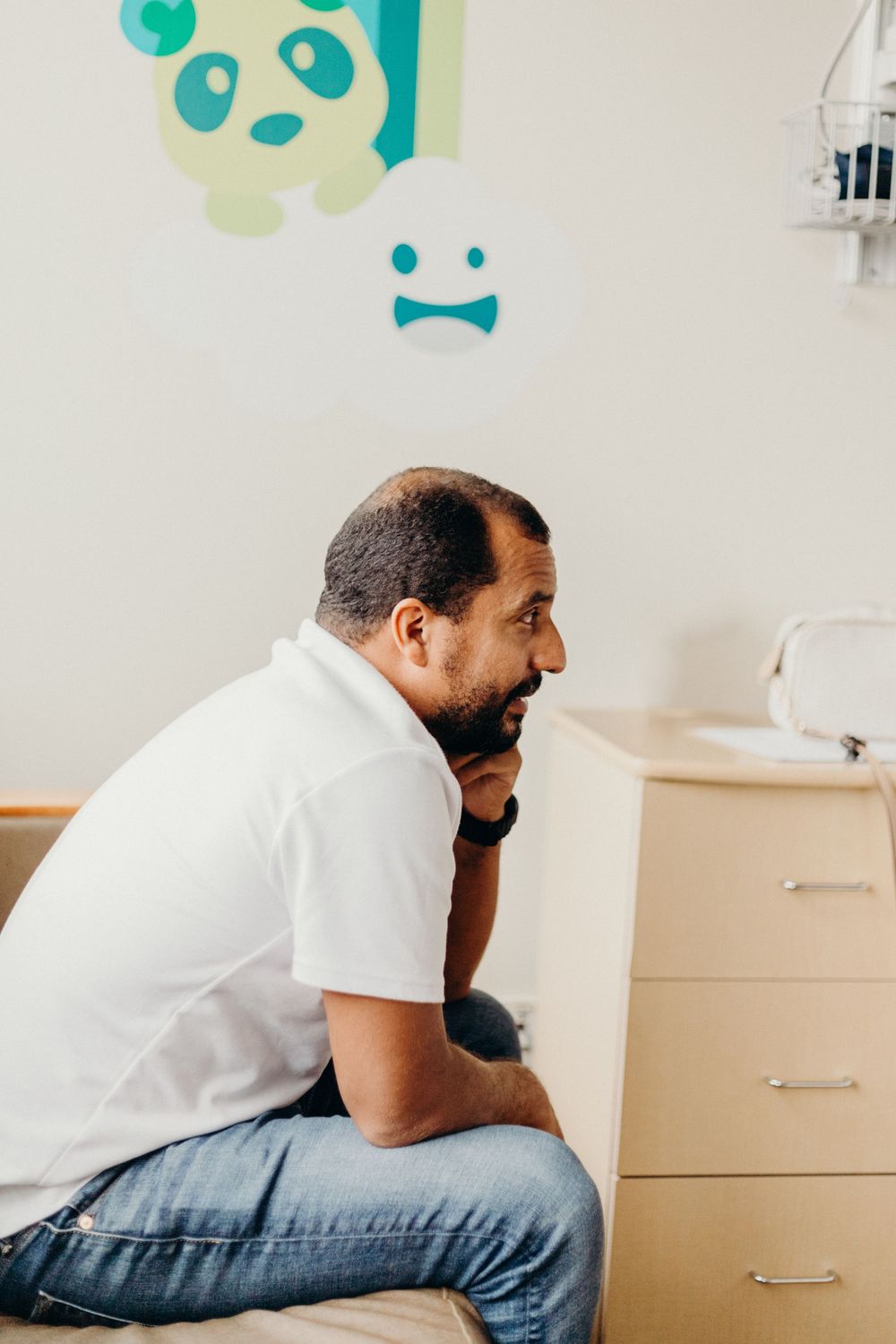 A medical professional in a white shirt leans over a hospital bed during a patient consultation.