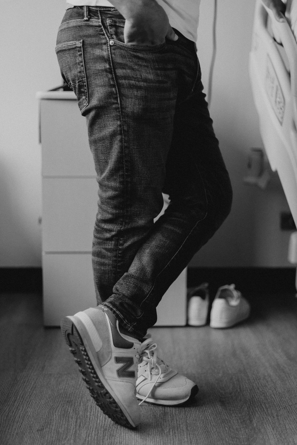 Black and white photo series showing feet in jeans and sneakers making small dance or movement steps on wooden floor.