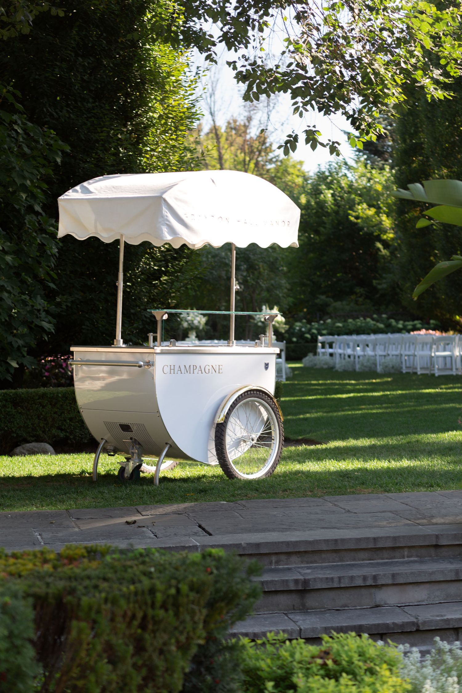 White vintage-style cart with a canopy sits on a wooden deck in a garden setting.