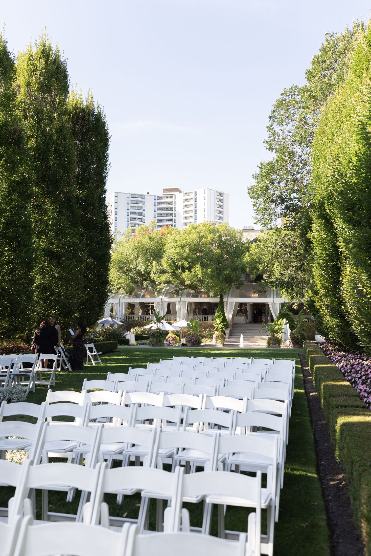 White folding chairs arranged in rows on a manicured lawn for an outdoor wedding ceremony with trees in the background.