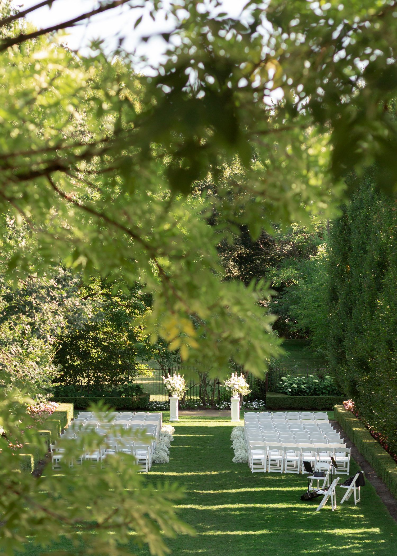 White chairs arranged in rows for an outdoor garden wedding ceremony under green leafy trees.