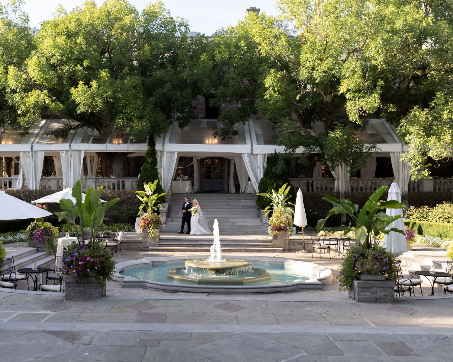 Panoramic view of a serene courtyard featuring a central fountain surrounded by lush trees and stone pathways.