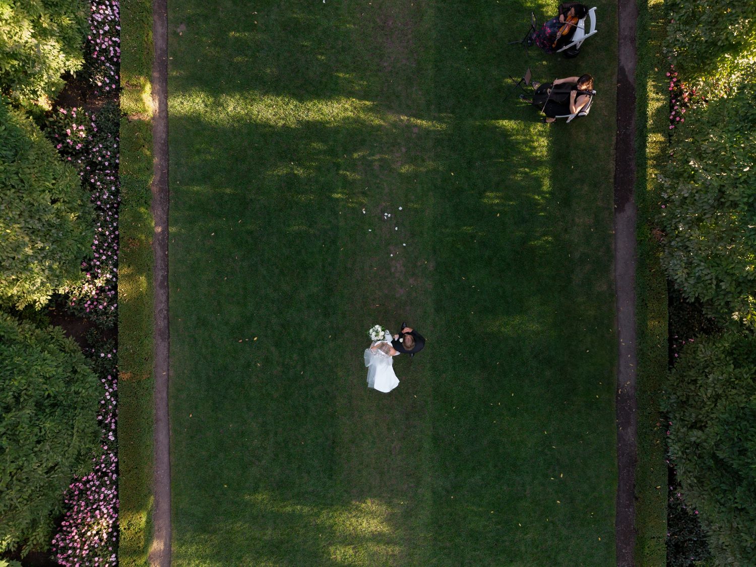 A person in a white dress walks down a grassy path lined with trees in a park-like setting.