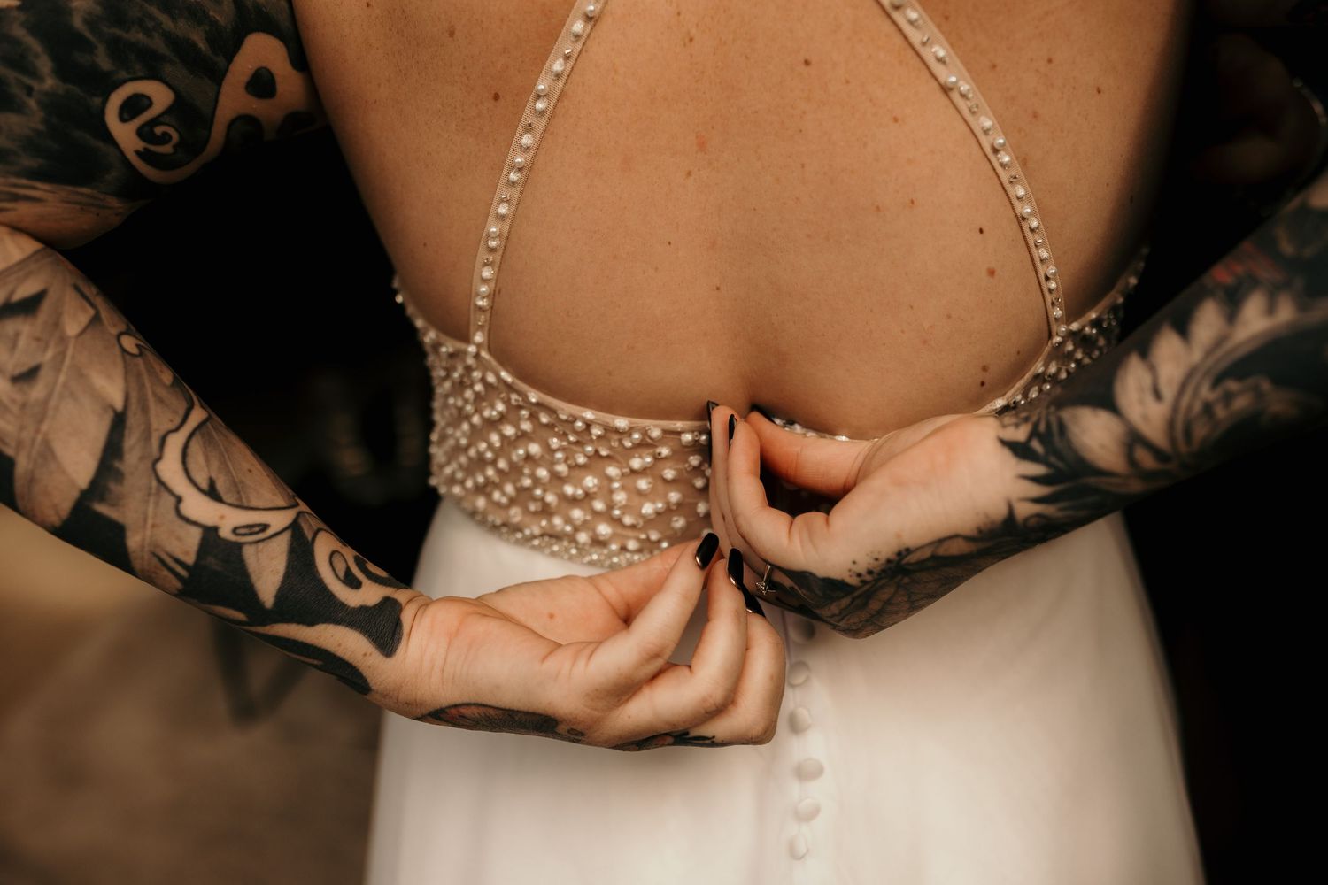 Close-up view of hands holding a pearl necklace against a dark background with elegant wedding attire.