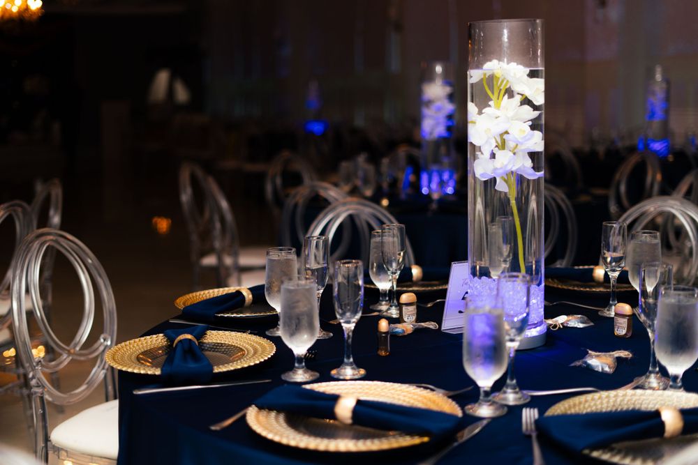 Formal dining table setup with navy and gold place settings under ambient lighting.