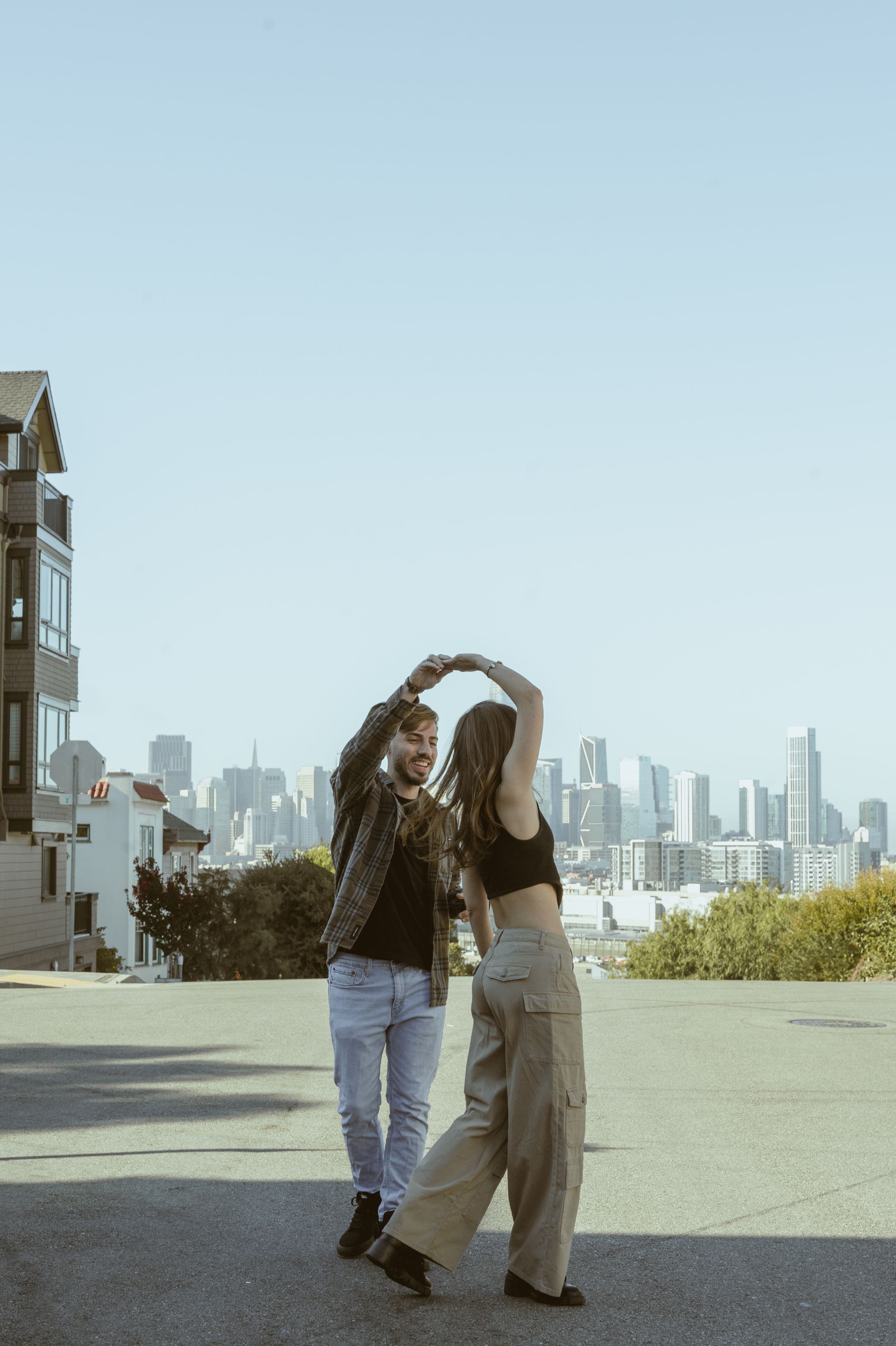 Couple walking together with San Francisco skyline visible in background on sunny day.