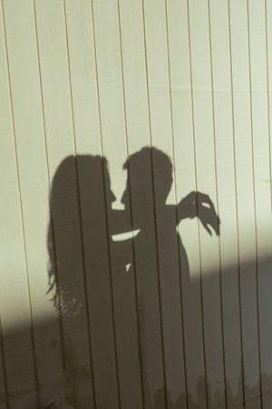 Shadow silhouette of embracing couple projected on striped wall.