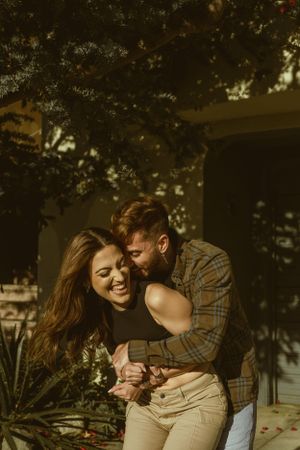 Joyful couple sharing laughter in warm afternoon sunlight near foliage.