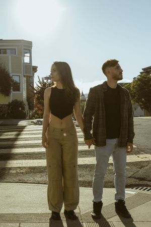 Two people hold hands while standing on a crosswalk during golden hour in a city street.