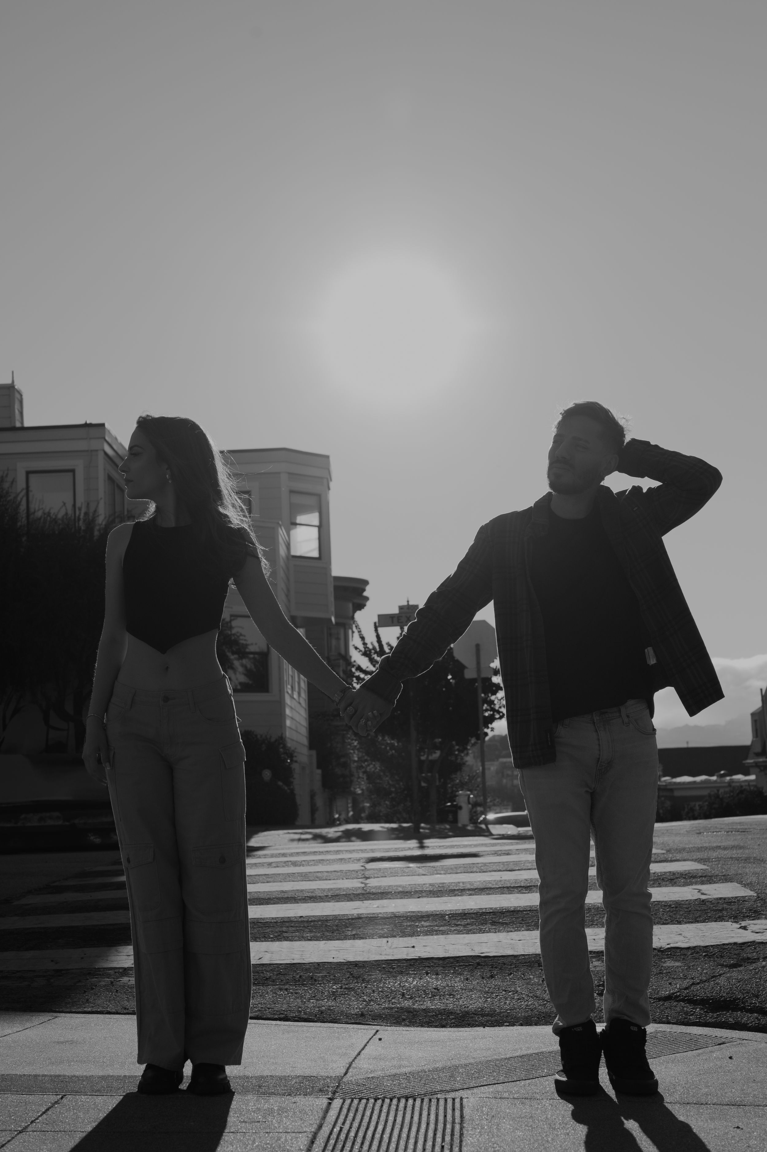 Silhouettes of a couple standing on a crosswalk during sunset with urban architecture in the background.