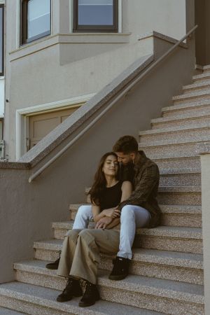 Intimate couple sitting together on outdoor steps in casual attire.