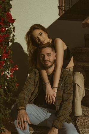 Romantic couple posing near red flowers in warm sunset lighting.