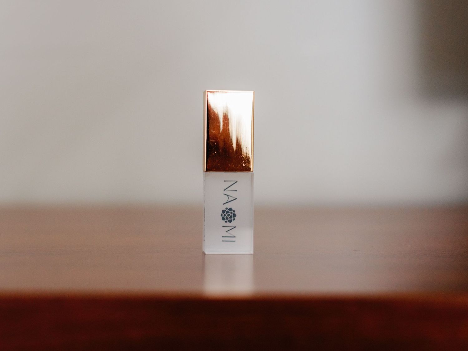 A minimal product shot of a white cosmetic bottle with rose gold cap against gray background.