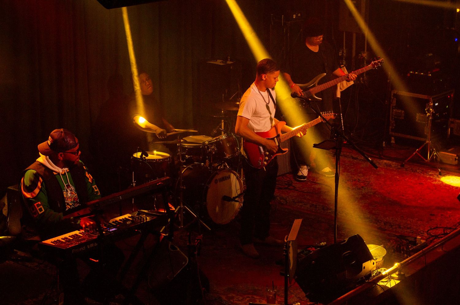 Band performing on stage with dramatic yellow lighting and smoke effects.