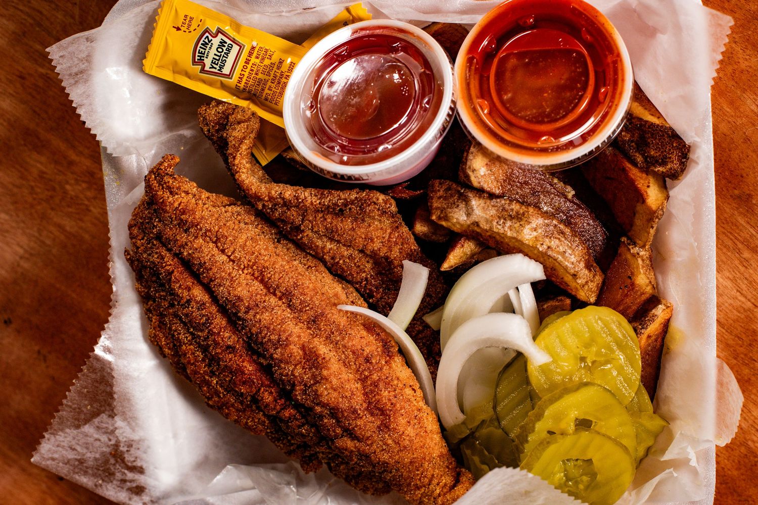 Crispy fried fish with pickles, onions and dipping sauces served on paper.