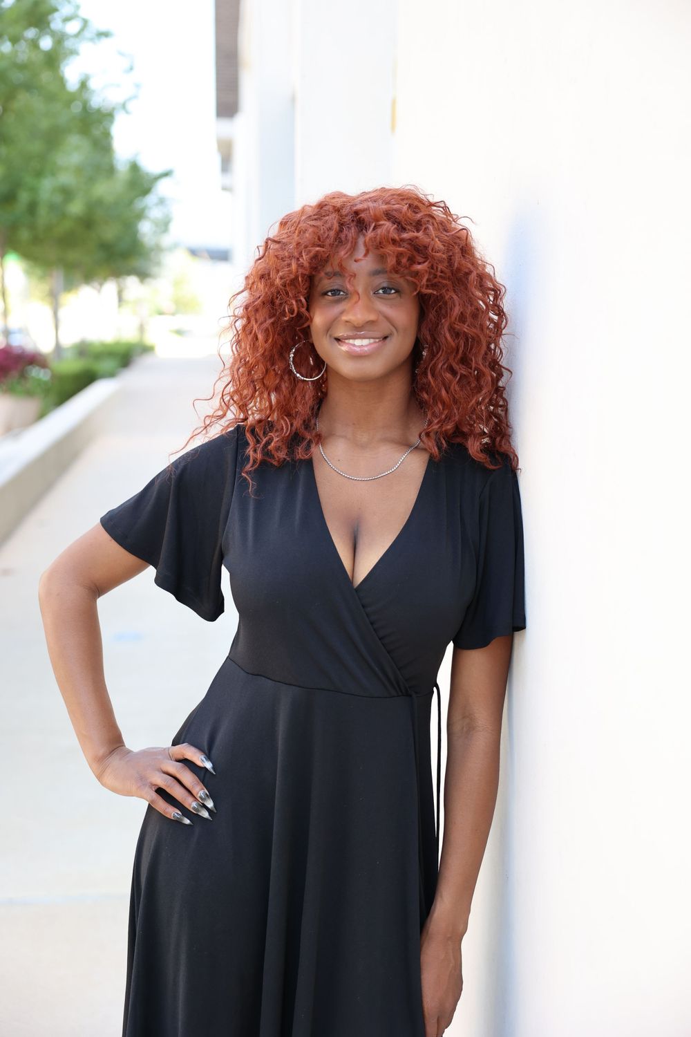 Portrait of woman in black wrap dress with natural red curls against white background.