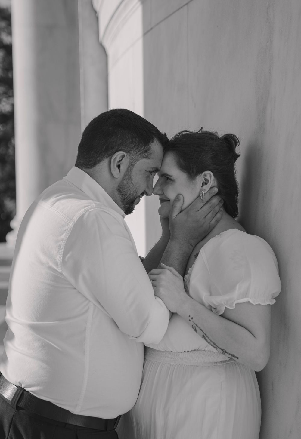 Black and white photo of a romantic couple sharing an intimate moment, man tenderly holding womans face near a column.