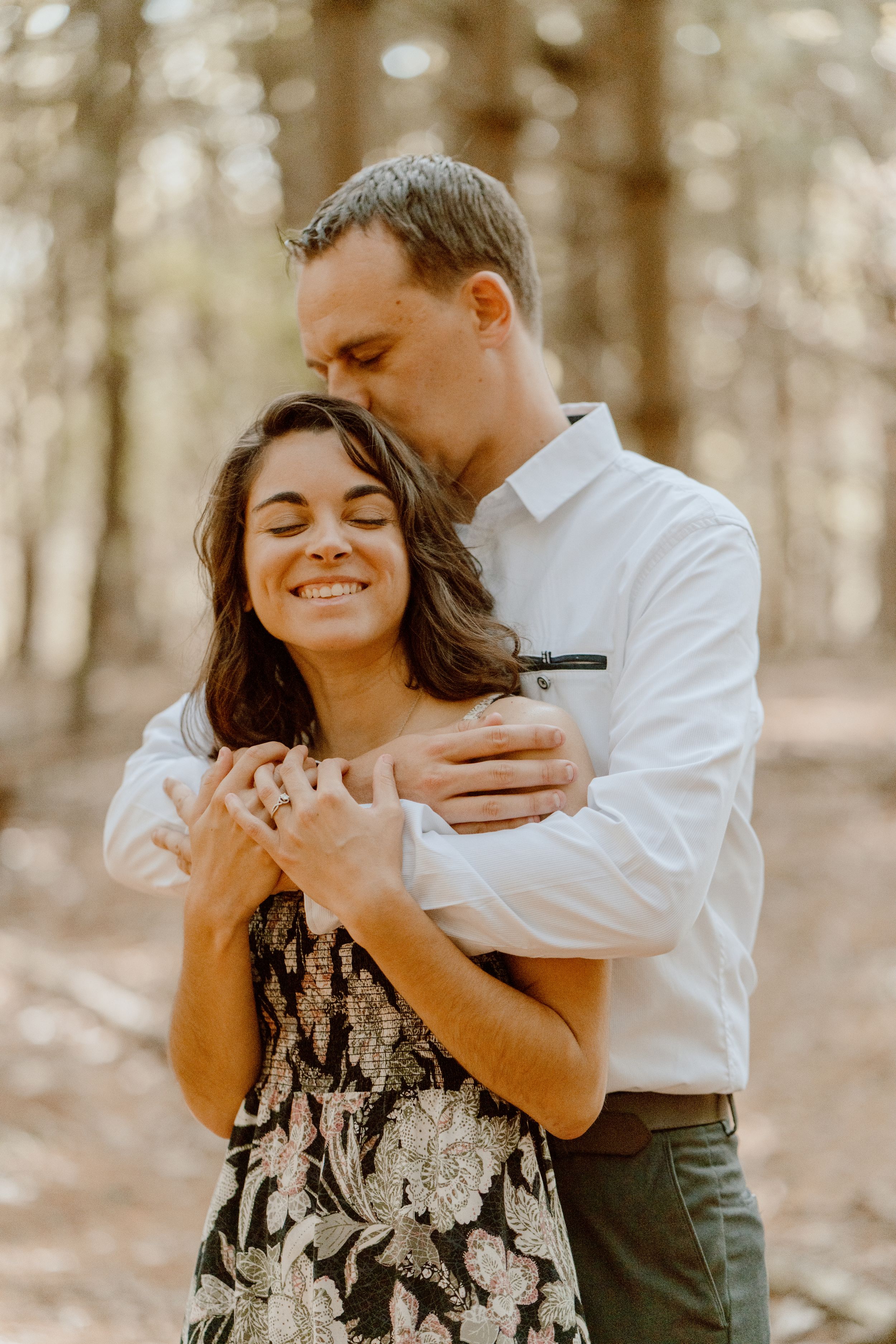 A couple shares joyful laughter during an intimate forest photoshoot.