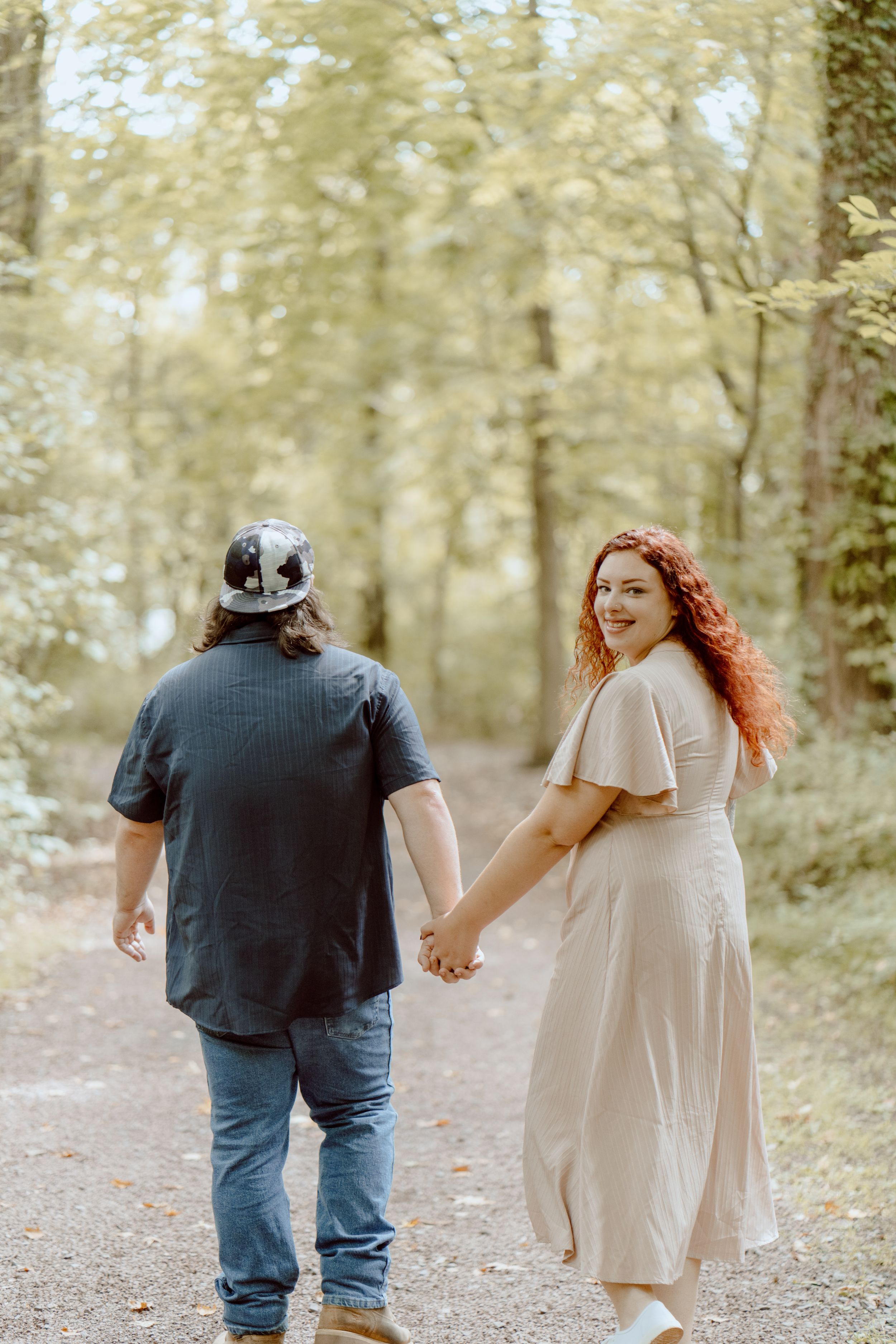 Couple walking hand in hand on a wooded trail in autumn light.