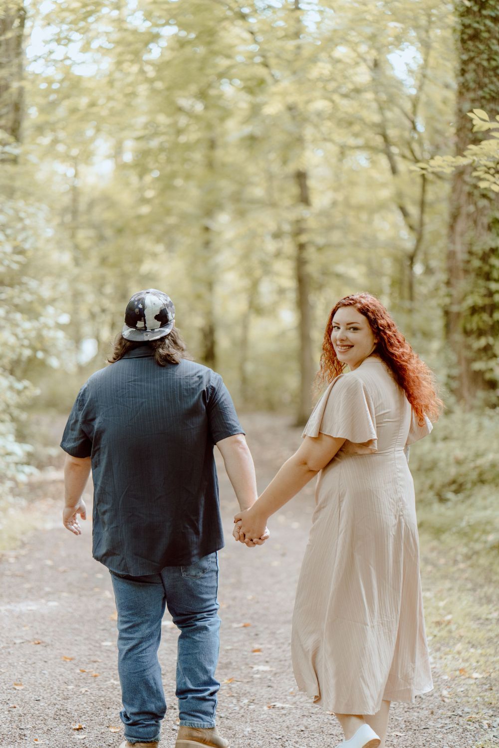 Couple walking hand in hand on a wooded trail in autumn light.