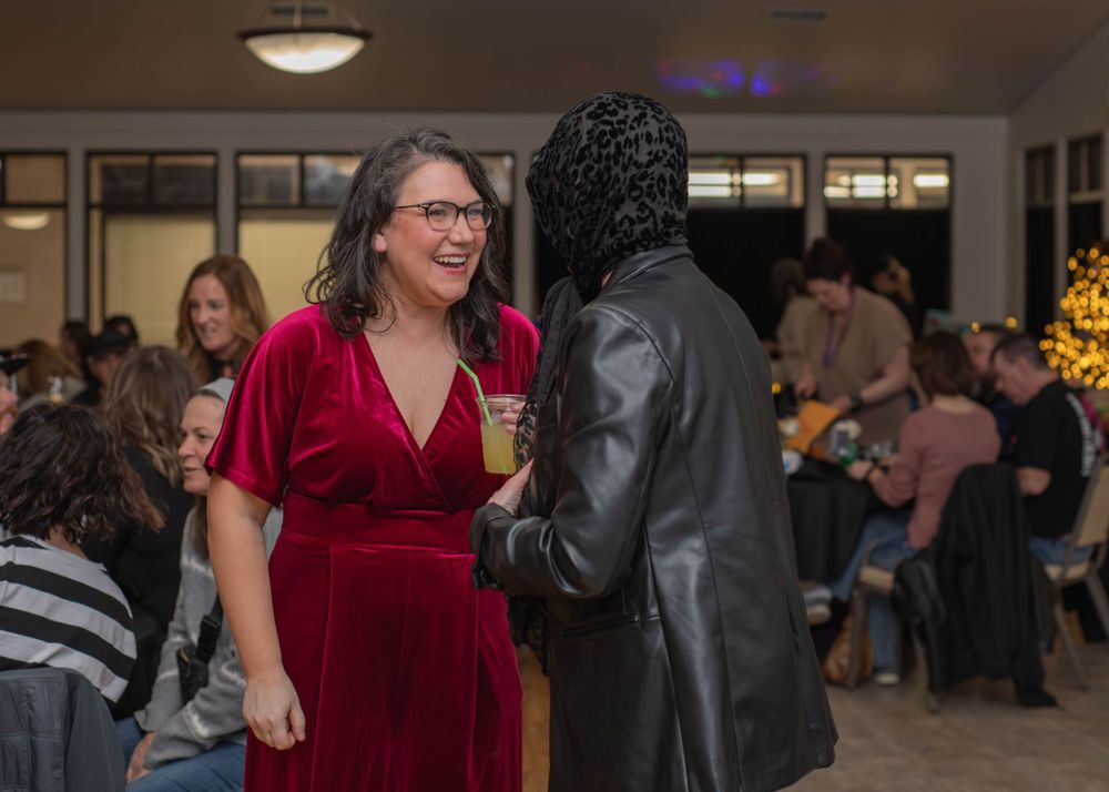 Woman in red velvet dress smiling and conversing with another guest at a holiday party.