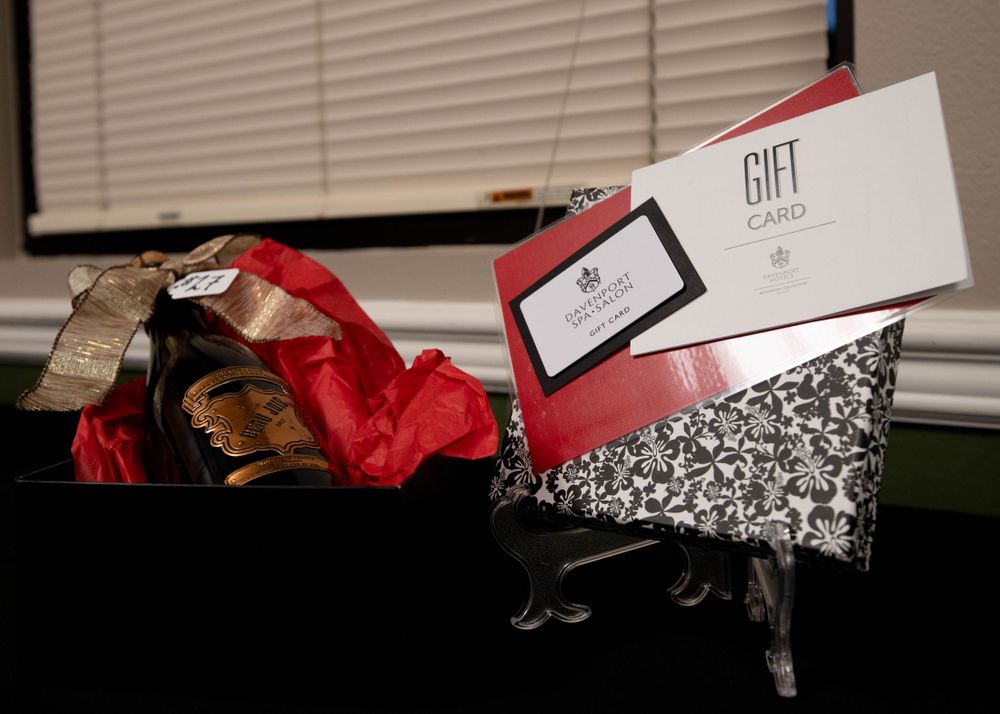Gift basket with red tissue paper and gift card displayed on a decorative black stand.