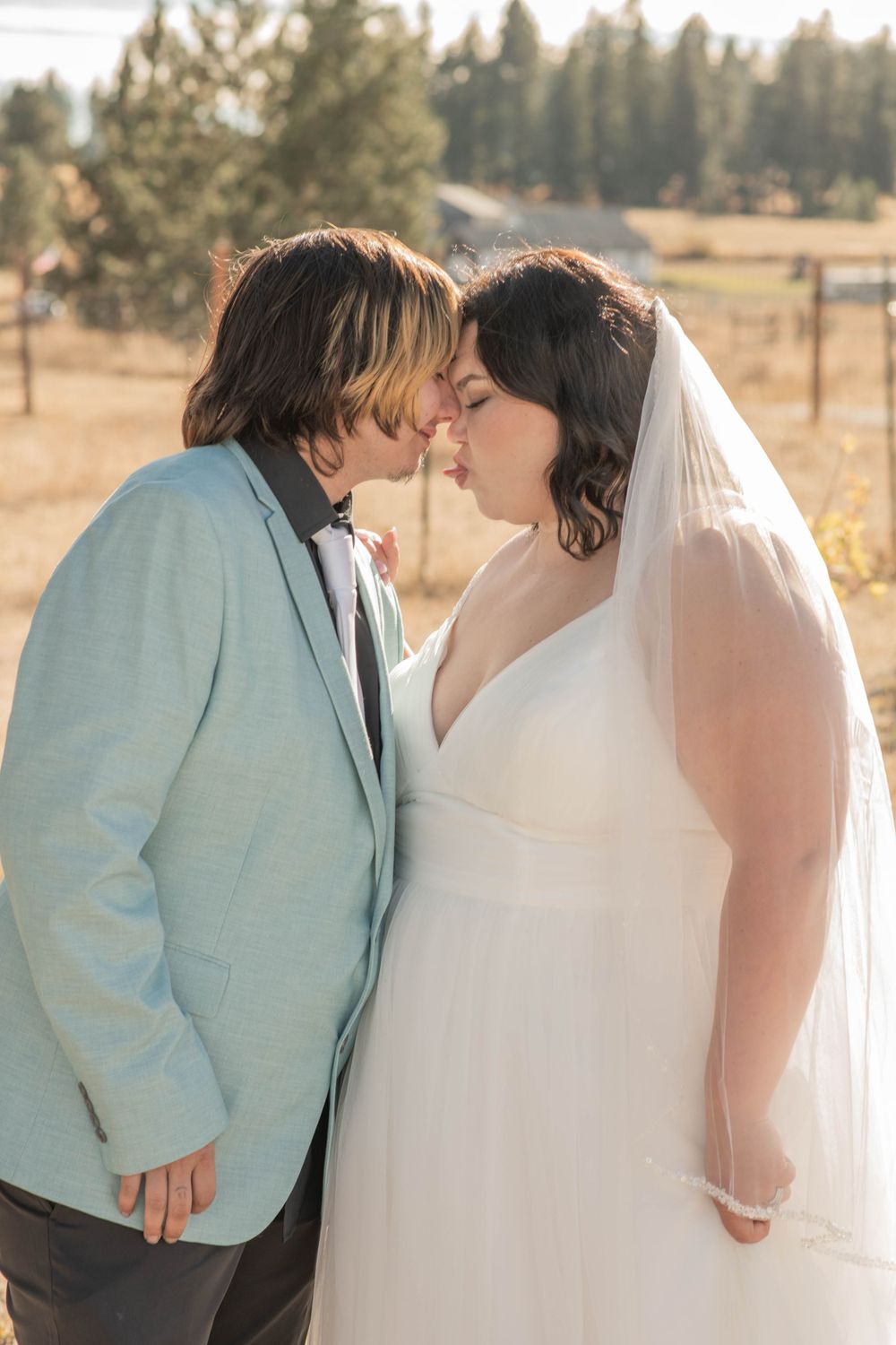 Bride and groom sharing a tender almost-kiss on their wedding day outdoors with scenic countryside background.