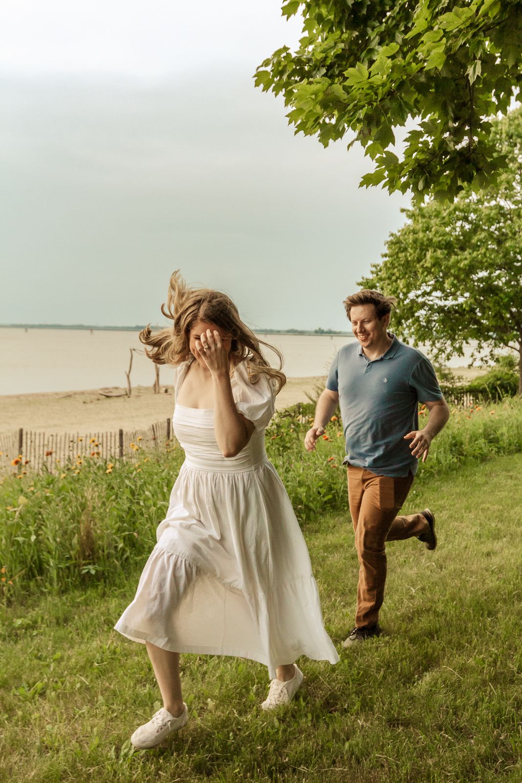 Couple running playfully through grass near beach on overcast summer day.