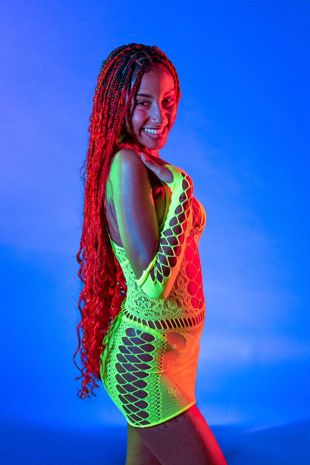 Colorful portrait with neon lighting featuring person in green mesh dress against blue background.