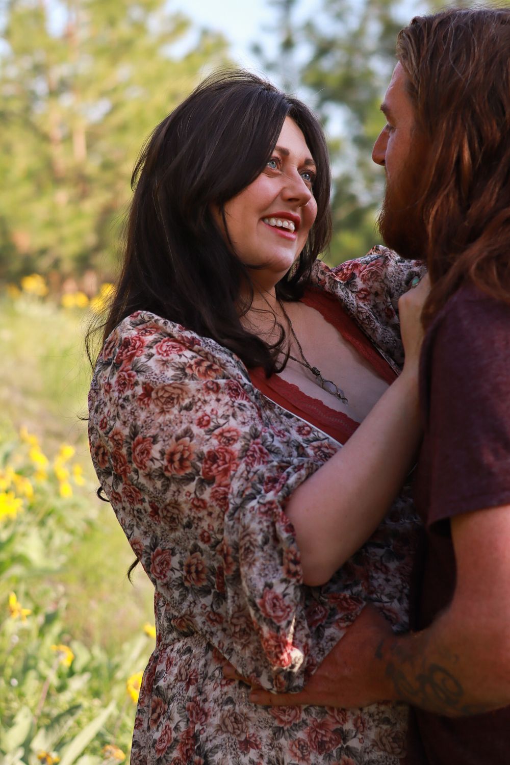Two people sharing a joyful moment outdoors wearing floral and casual clothing against a natural background.